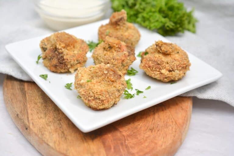 Keto air fried mushrooms served on a white plate with parsley and creamy dipping sauce.