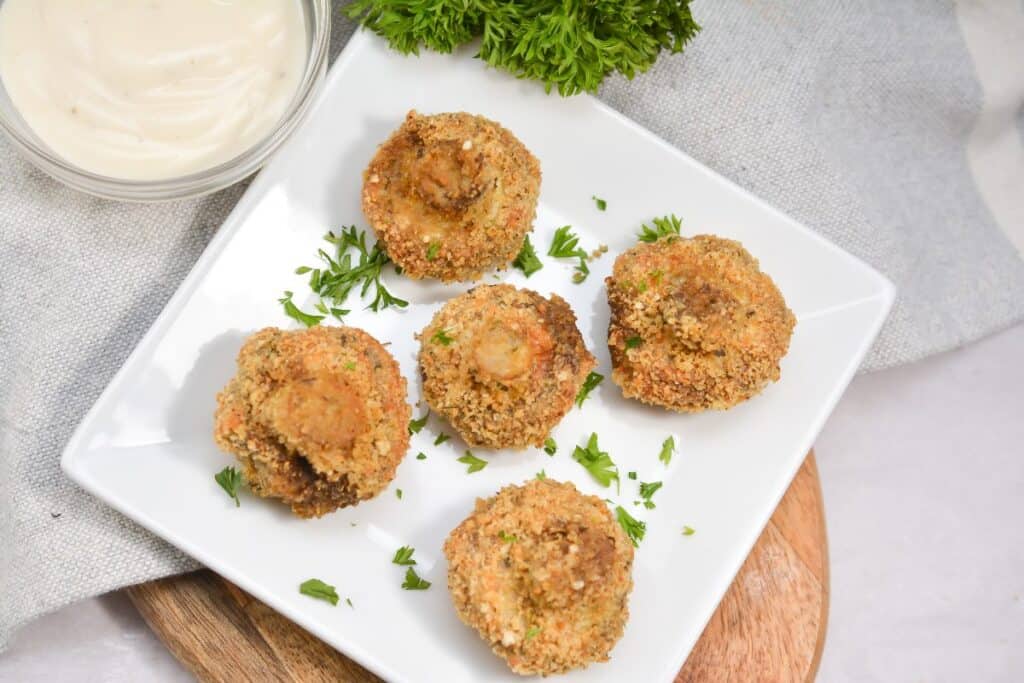 Keto air fried mushrooms appetiser served on a white plate with parsley and creamy dipping sauce.