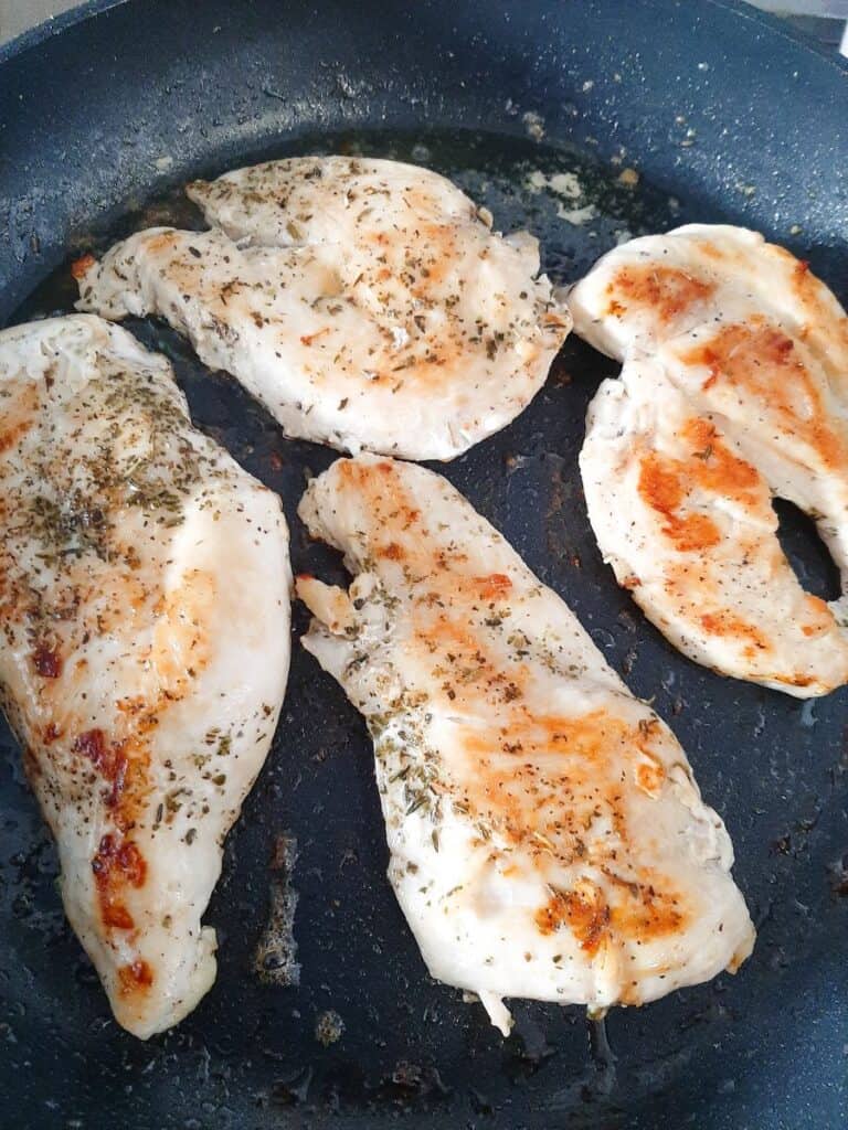 Chicken pieces browning in a skillet for keto chicken with sun-dried tomato sauce.
