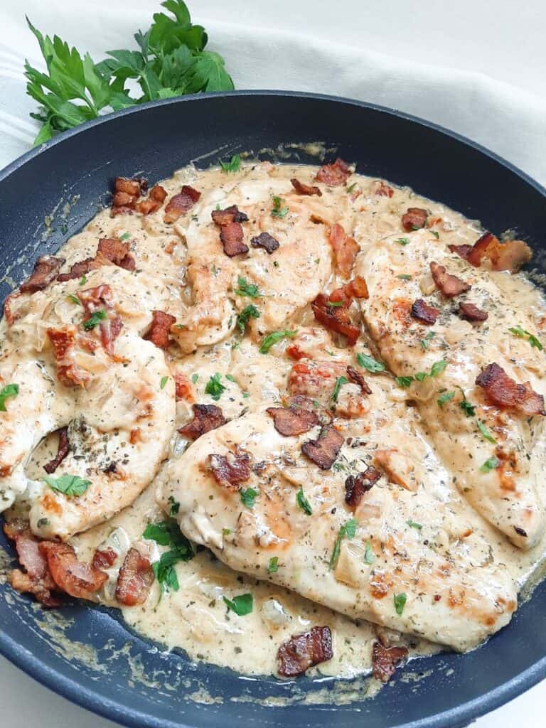 Keto chicken with sun-dried tomato sauce and bacon cooking in a skillet.