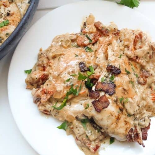 Keto chicken with sun-dried tomato sauce and bacon served on a white plate.