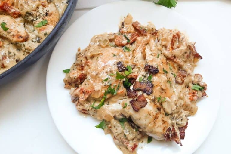 Keto chicken with sun-dried tomato sauce and bacon served on a white plate.